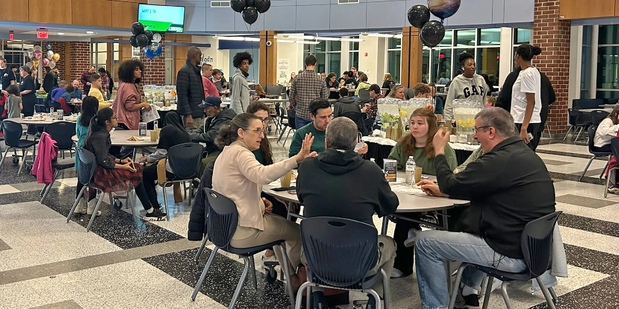 Photo of a school commons area with people sitting and eating at cafeteria tables