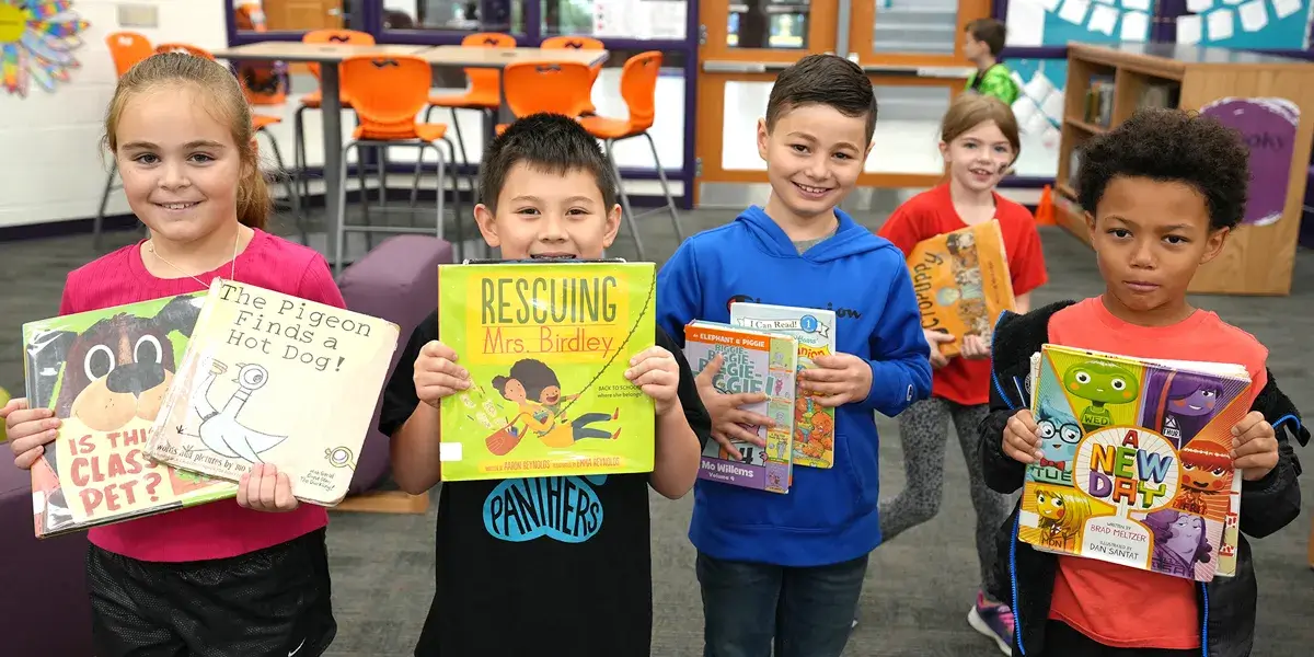 Five elementary school students holding books standing in their school library