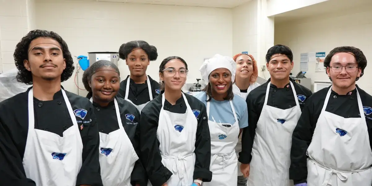 Superintendent McDade wearing a chef's apron while posing for a photo with students enrolled in the culinary program at Potomac High School