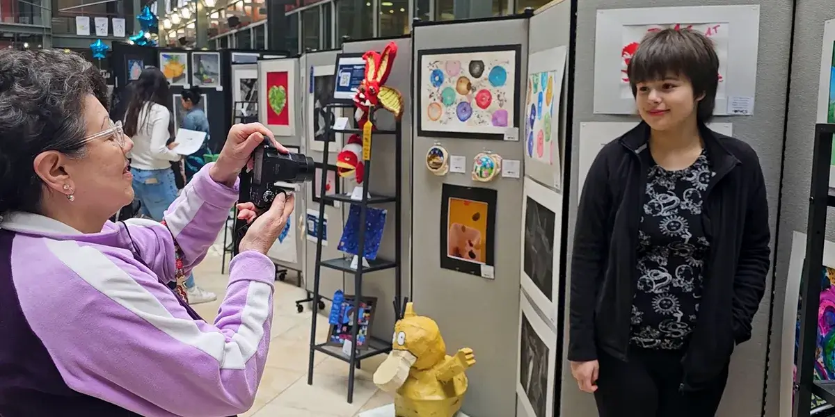 PWCS student posing for a photo while standing in front of her artwork at an All-County Fine Arts festival