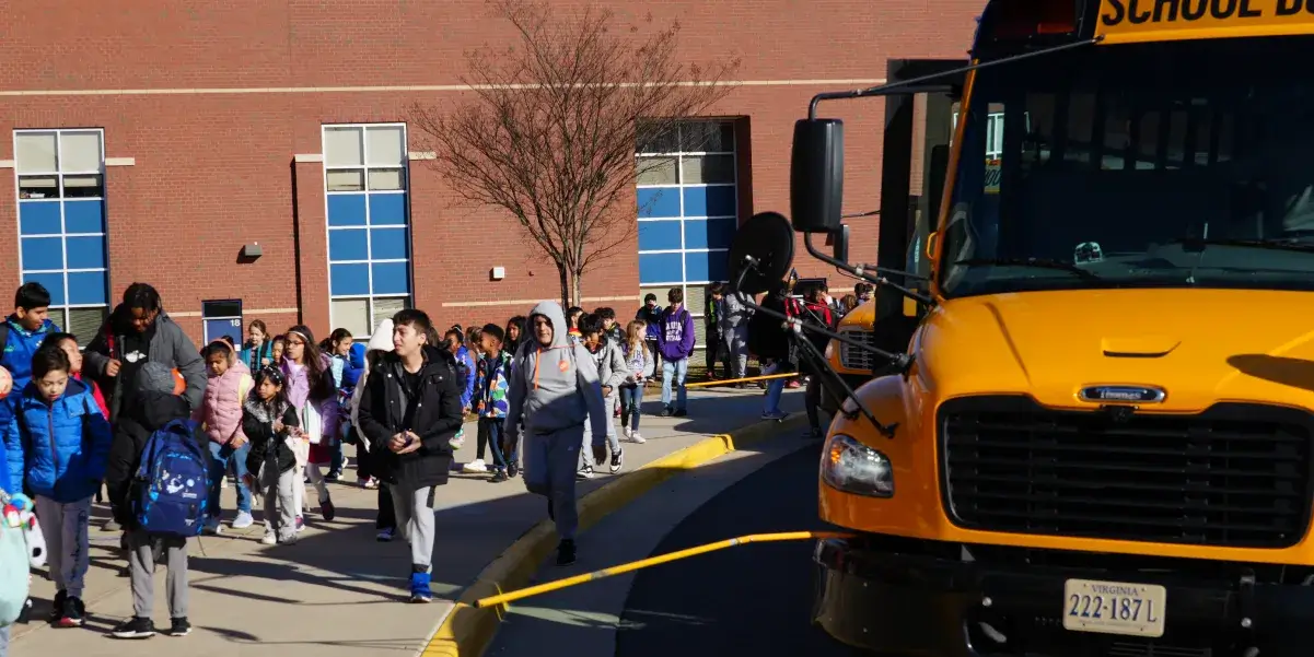 Elementary school students walking in front of school buses after arriving at school