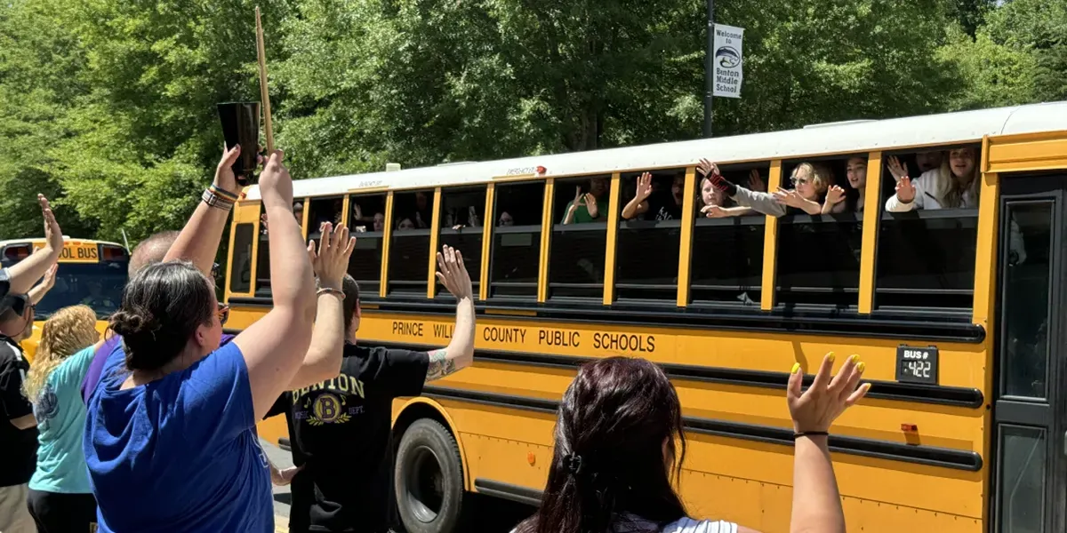 Teachers and staff at Benton Middle School waive to students on school buses on the last day of school