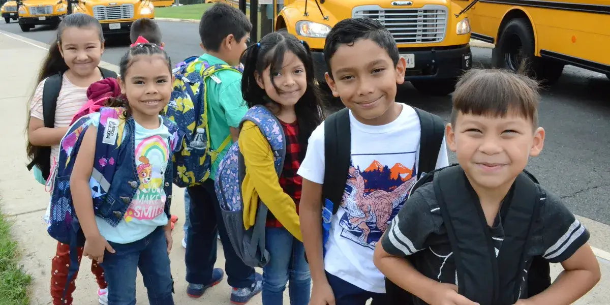 Group of elementary school students lined by in front of school buses