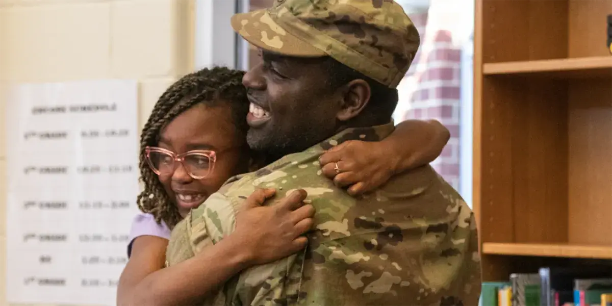 Military parent in uniform hugging their child in a classroom