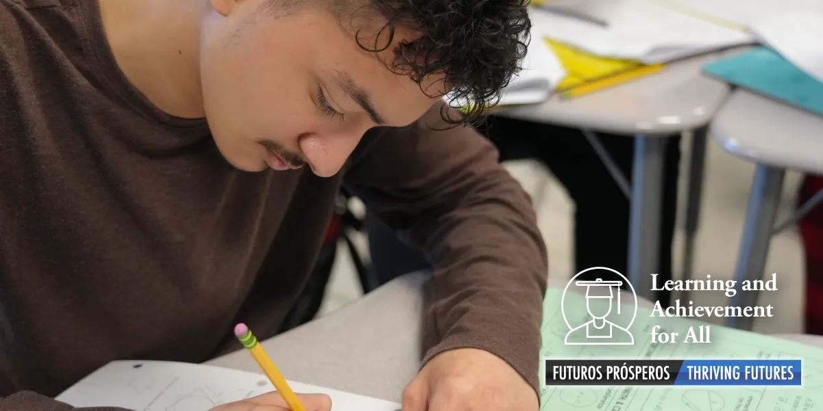 Student sitting at a desk writing while writing on paper with a pencil