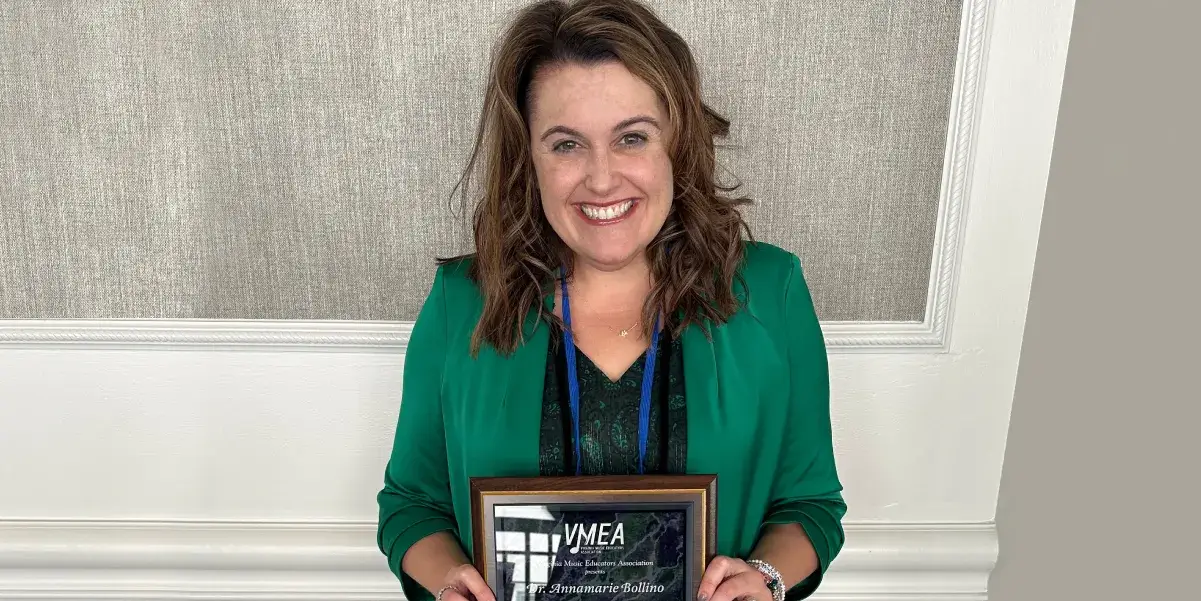 Smiling woman holding a framed award, wearing a green blazer and standing against a textured wall.