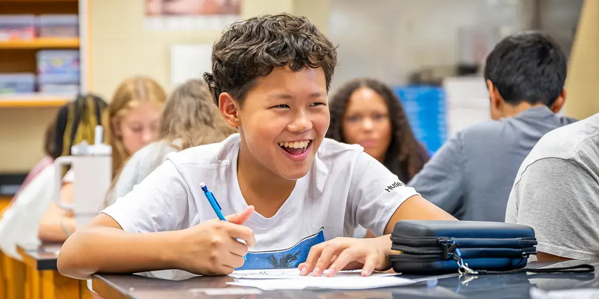 Middle school students sitting at desks in a classroom with one smiling student in the foreground