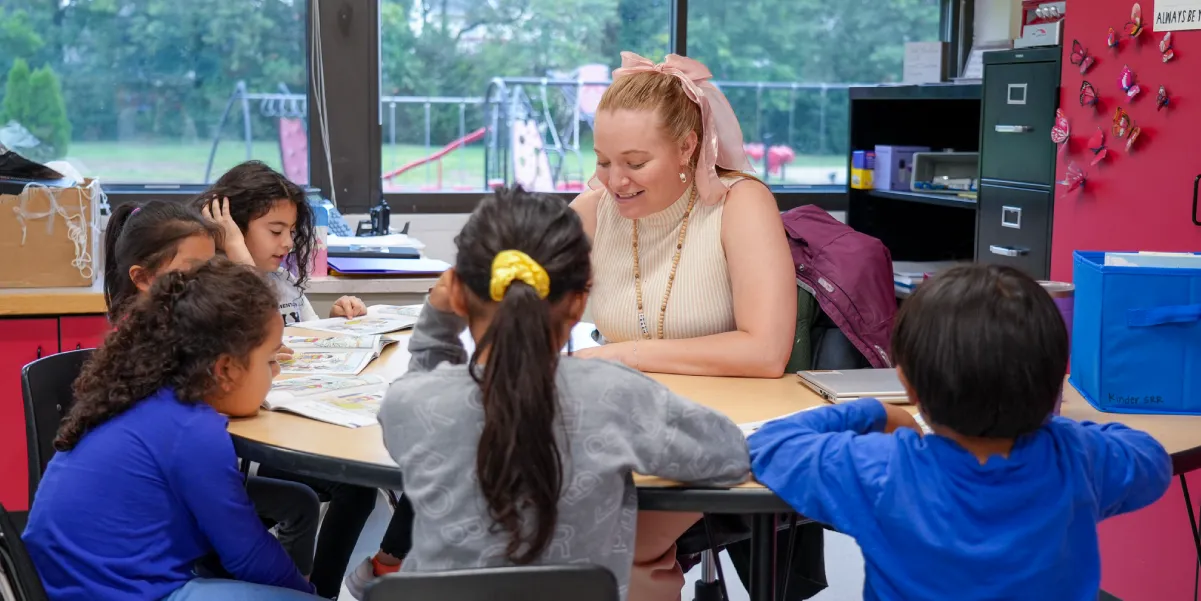 Elementary school teacher sitting at a half-moon shaped table with five students