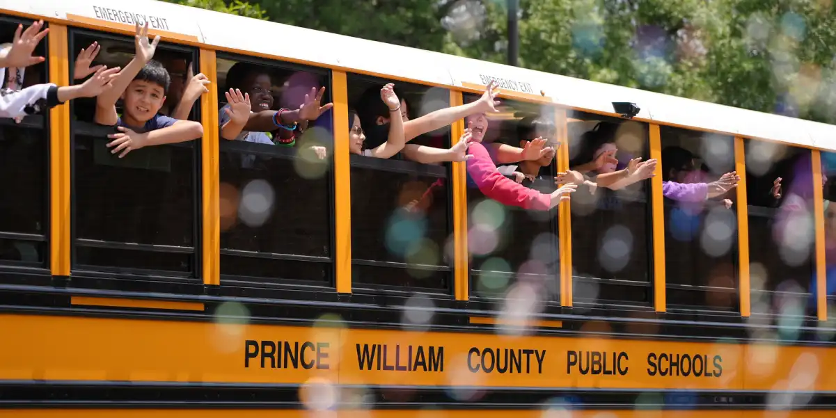 Students waving out the windows of a school bus on the last day of school