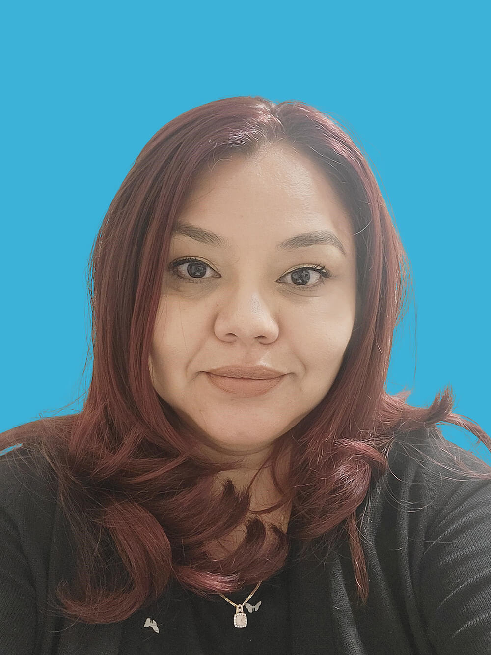 A woman with long, wavy red hair posing in front of a bright blue background. She is wearing a black cardigan and has a neutral expression.