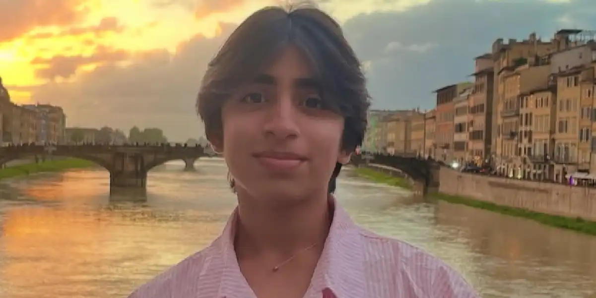 Deen Lateef by a river at sunset, with buildings and a bridge in the background.