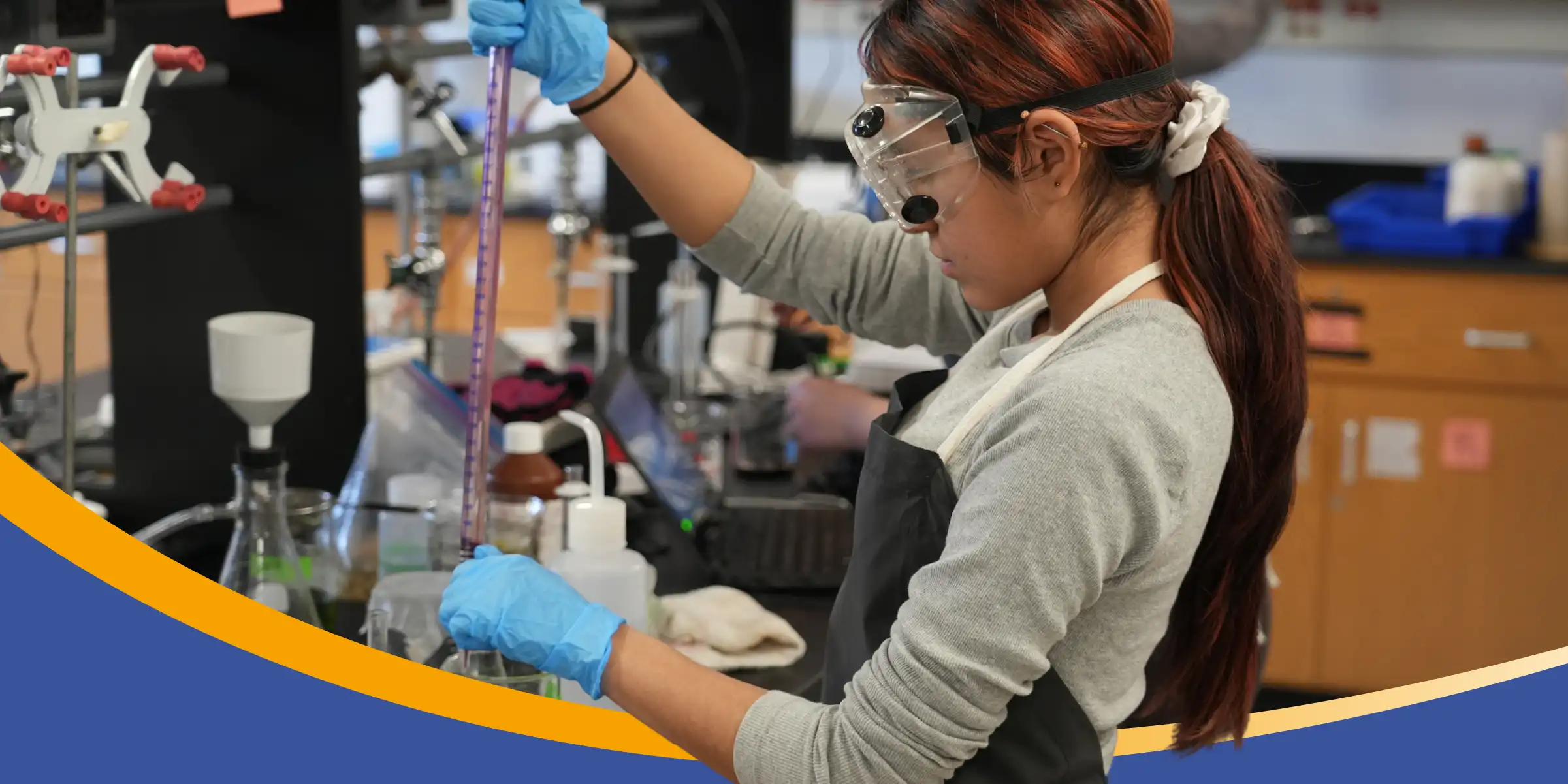 Student wearing safety goggles and gloves measures liquid in a graduated cylinder during a science lab experiment.