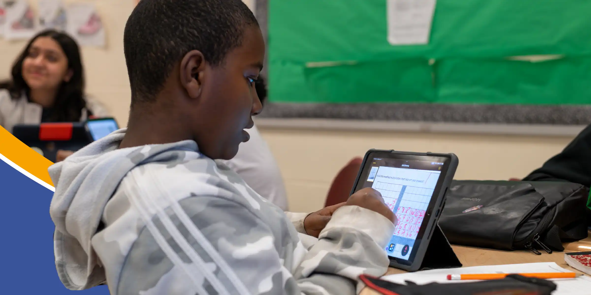 Student in a classroom working on a tablet with a math worksheet displayed.
