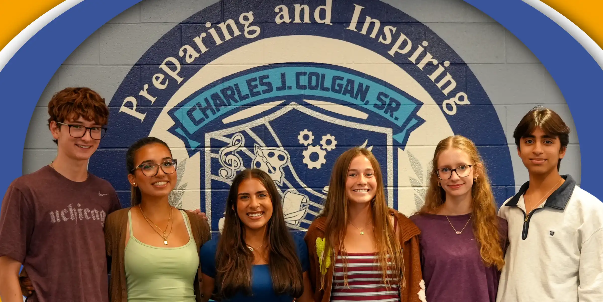 a group of six students standing smiling in front of a wall that reads "preparing and inspiring"