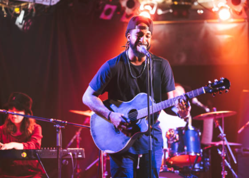 a musician on stage playing a guitar and singing. woman in background playing keyboard on stage