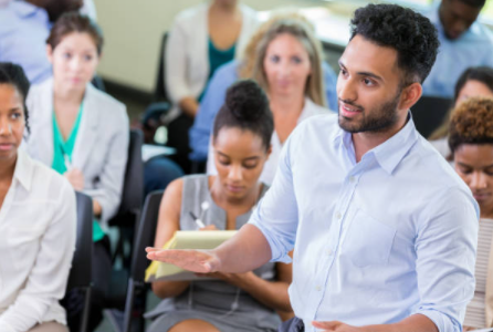 man speaking while standing at a meeting with a seated audience man speaking while standing at a meeting with a seated audience