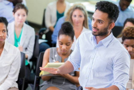 man speaking while standing at a meeting with a seated audience