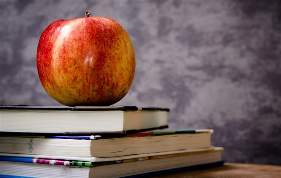 A red apple placed atop a stack of three textbooks
