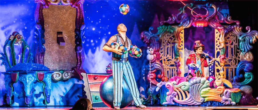 two colorfully dressed individuals on a decorated stage. one is juggling balls and the other is playing a stringed instrument