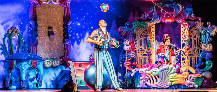 two colorfully dressed individuals on a decorated stage. one is juggling balls and the other is playing a stringed instrument two colorfully dressed individuals on a decorated stage. one is juggling balls and the other is playing a stringed instrument