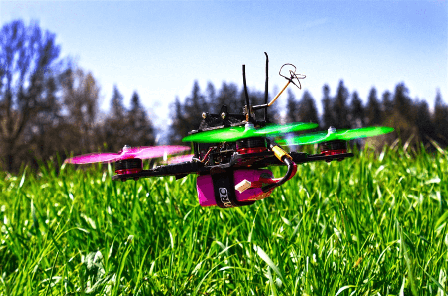 A pink and green drone hovering over grass