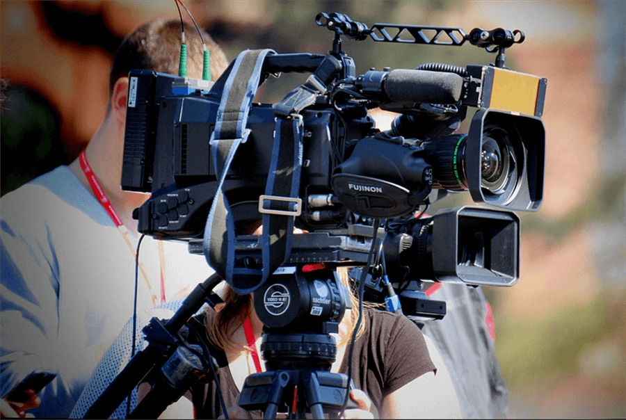 A camera used for filming video with a man and woman whose faces are obscured standing behind the equipment