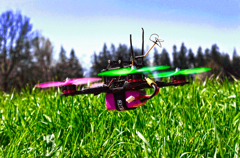 A pink and green drone hovering over grass