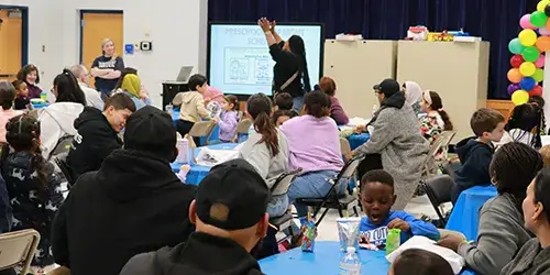 Families seated at tables at the beginning for a family engagement event