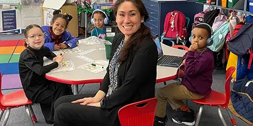 Elementary school teacher seated at a table with students in a classroom