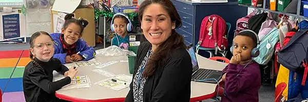 Elementary school teacher seated at a table with students in a classroom