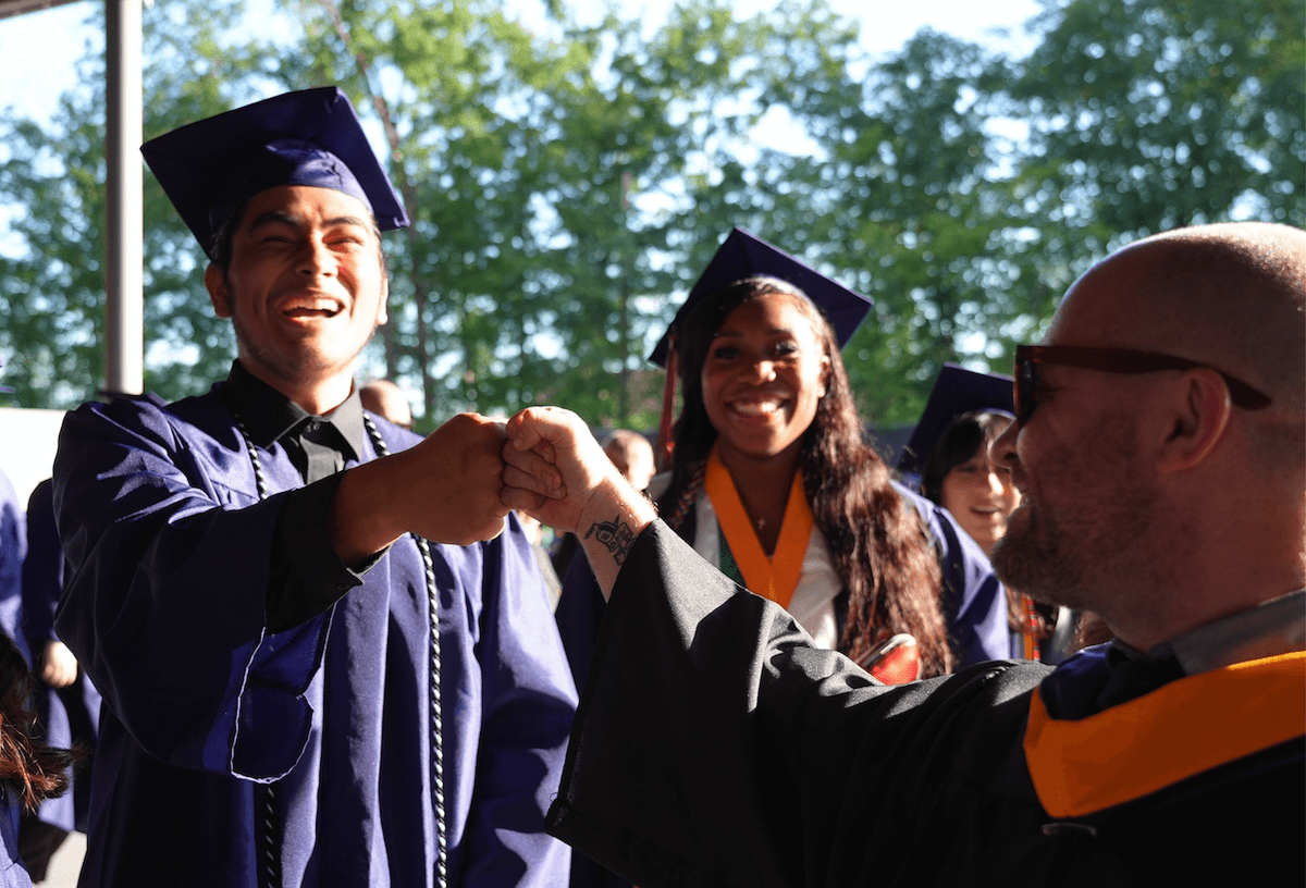 a high school graduate fist-bumping a faculty member at graduation ceremony