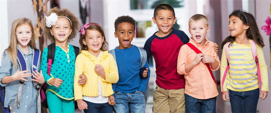 Group of seven elementary school girls and boys standing walking in the hall with smiles on their faces