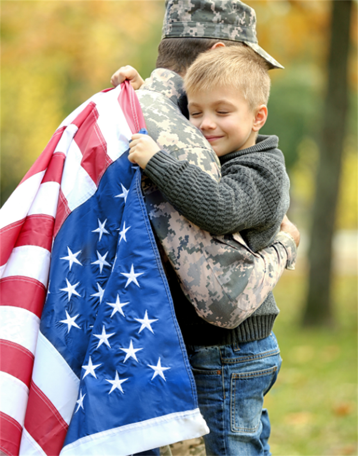 Photo of young boy hugging a military soldier draped in the American flag