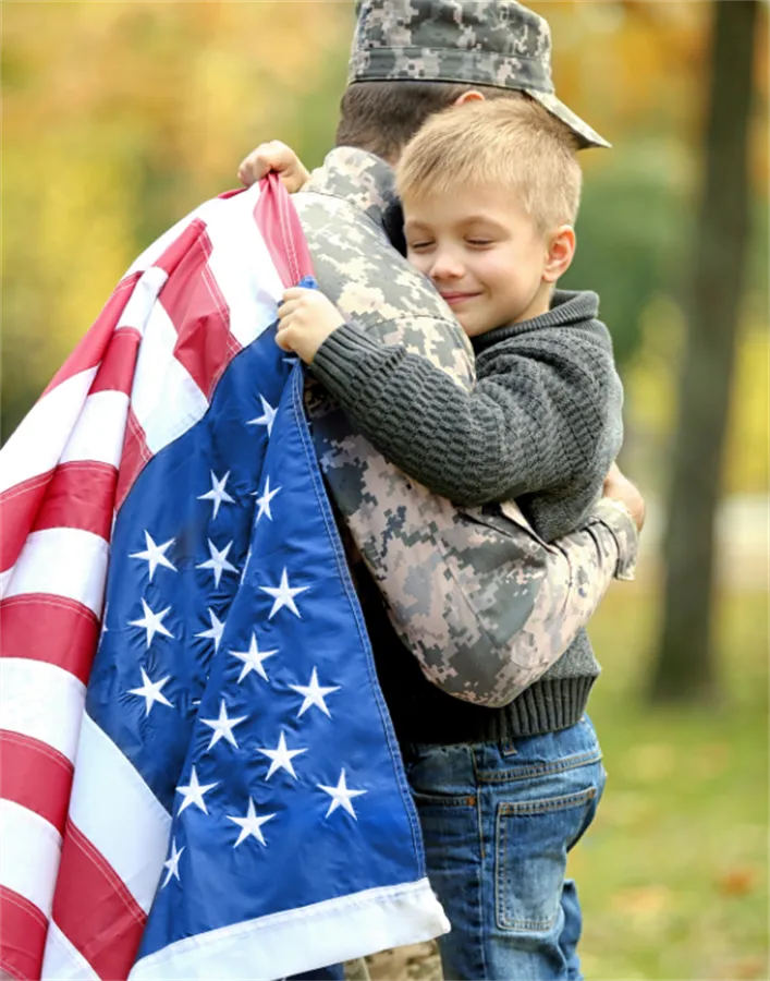 Young boy hugging a military soldier draped in the American flag