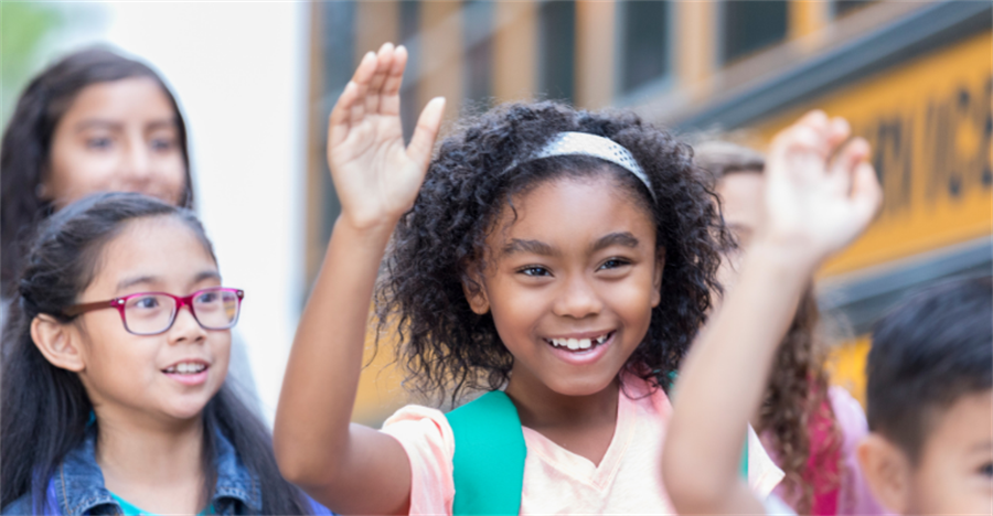 Smiling children walking next to school bus with hands raised