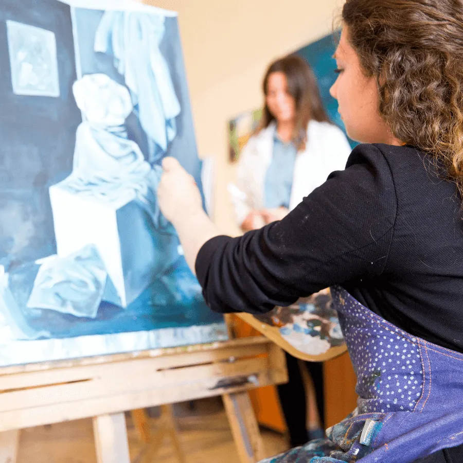 Student sitting and painting on an easel