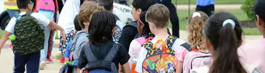 Elementary school students wearing backpacks walking from bus